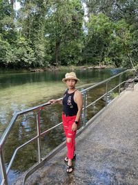 Full length portrait of woman standing by lake against trees