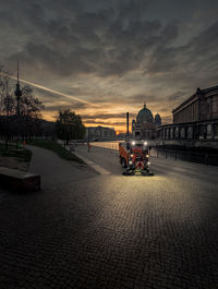 Cars on street by buildings against sky during sunset