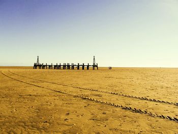 Pier at sandy beach against clear sky