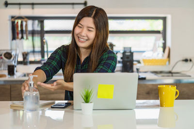 Portrait of young woman using mobile phone while sitting on table