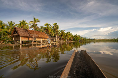 Wooden house by lake and trees against sky