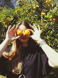 Young woman holding oranges on her face against tree at farm