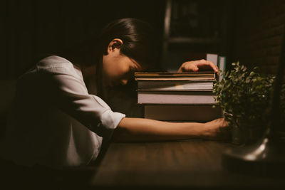 Side view of young woman relaxing by books on table at home