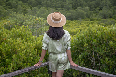 Rear view of woman standing by railing against forest