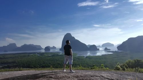 Rear view of man with hand in pocket standing against sky