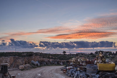 Empty road by abandoned bulldozer and tires at junkyard during sunset
