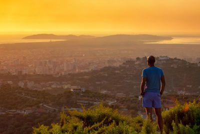 Rear view of man looking at cityscape against sky during sunset