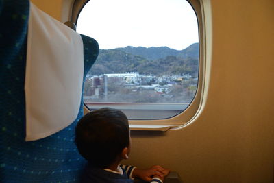 Rear view of boy looking through window