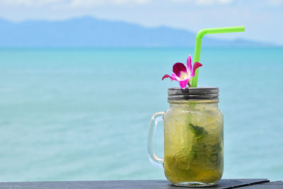 Close-up of mojito cocktail in glass jar on table against sea