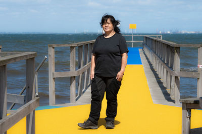 Portrait of young man standing on railing against sea