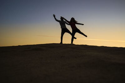 Silhouette people dancing on land against sky during sunset