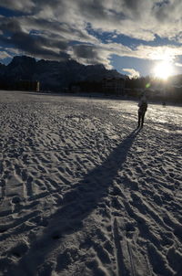 Person standing on sand at beach against sky during sunset