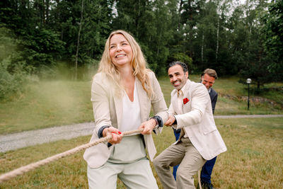 Smiling male and female colleagues pulling rope while playing tug-of-war in lawn