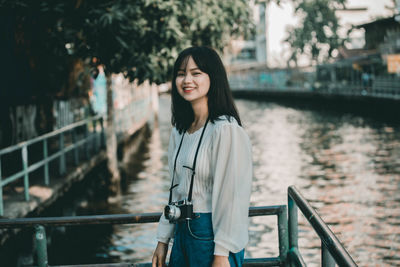 Portrait of smiling young woman standing by railing