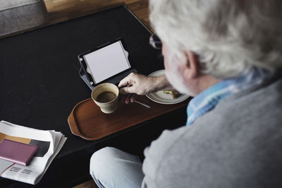 Cropped image of senior man holding tea cup by digital tablet at table