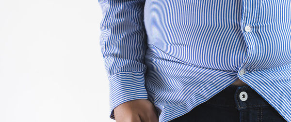 Midsection of man wearing striped shirt while standing against white background