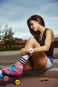 Young woman with skating shoe sitting outdoors