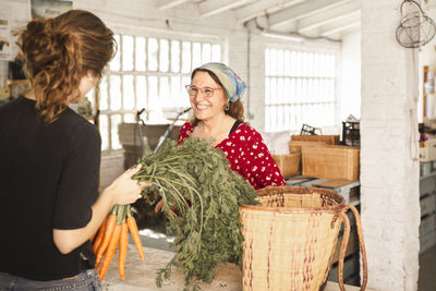 Happy customer talking with grocer holding carrots in shop