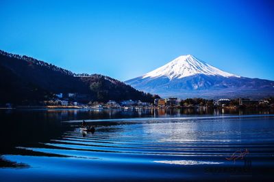 Scenic view of lake and snowcapped mountains against clear blue sky