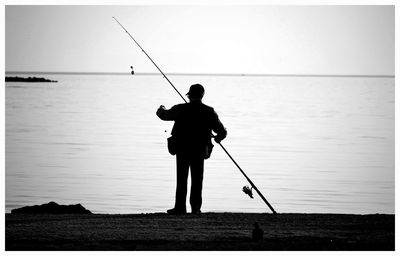 Rear view of silhouette man fishing in sea