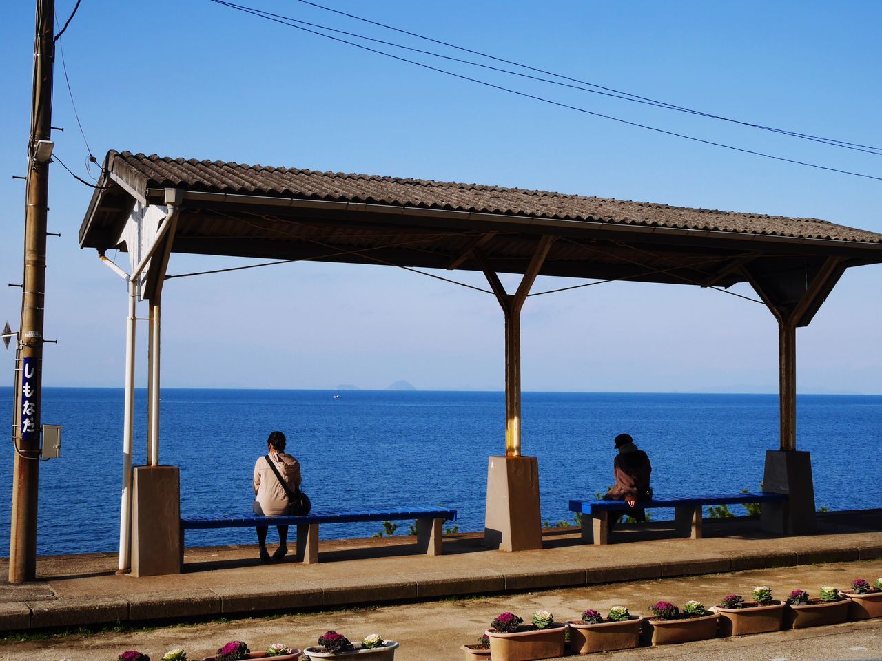 sea, water, horizon over water, clear sky, real people, rear view, men, nature, scenics, day, blue, leisure activity, sky, sitting, outdoors, beauty in nature, built structure, full length, lifestyles, architectural column, women, architecture, one person, fishing pole, people