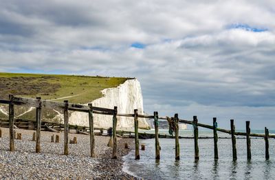 Wooden post on fence by land against sky