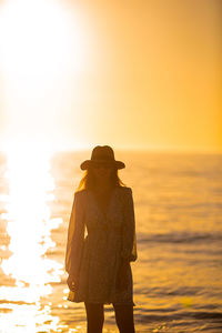 Rear view of woman standing against sea during sunset