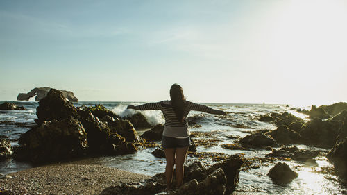 Rear view of woman standing on rock by sea against sky