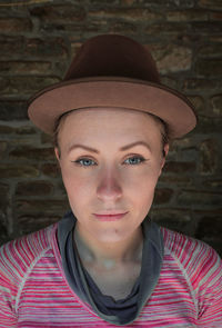 Close-up portrait of woman in hat against brick wall