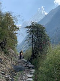 Rear view of person walking on footpath by mountain against sky