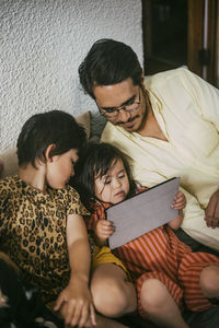 Down syndrome daughter using digital tablet by father and sister on sofa at home