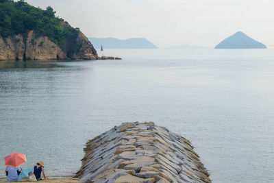 People on rocks by sea against sky