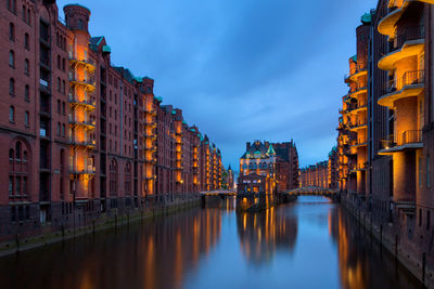 Canal amidst buildings against sky at dusk