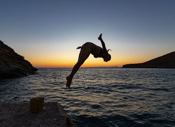 Silhouette of jumping in sea against sky during sunset