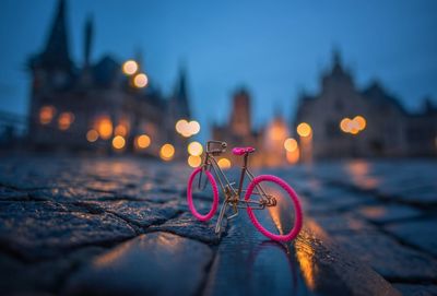 Close-up of pink bicycle model on cobbled street against illuminated buildings at night