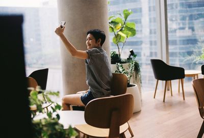 Woman taking selfie through mobile phone against window