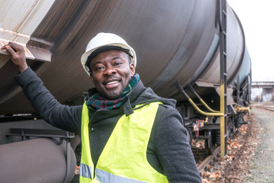 Smiling african american mechanic wearing safety equipment, helmet and jacket, looking at camera