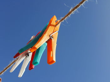 Low angle view of clothespins hanging against clear blue sky