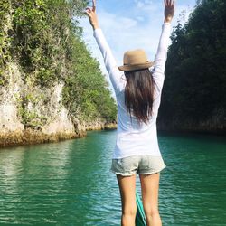 Rear view of woman with arms raised on boat in river