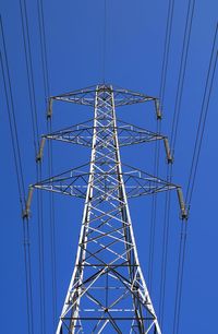 Low angle view of electricity pylon against clear blue sky