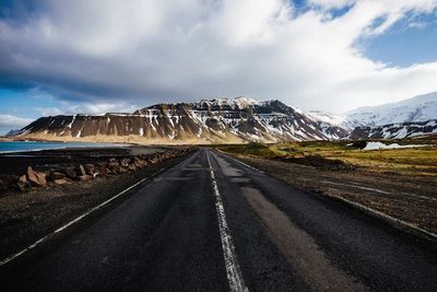 Road leading towards mountain against cloudy sky