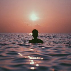 Silhouette man swimming in sea against sky during sunset