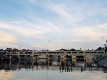 Buildings by river against sky during sunset