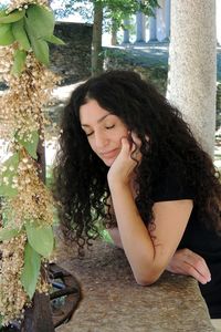 Beautiful young woman looking down while sitting on tree trunk