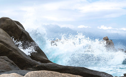 Waves splashing on rocks against sky