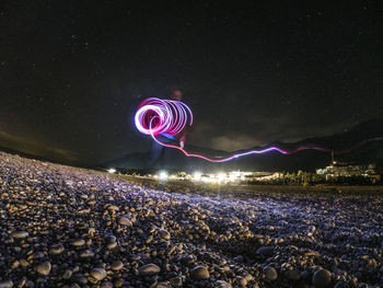 Illuminated light painting on rock in sea against sky at night