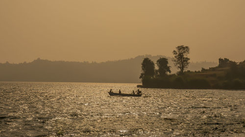 Silhouette boat by trees against clear sky during sunset
