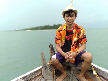 Portrait of smiling young man sitting on boat in sea against cloudy sky