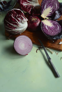  radicchio, knife, cut red cabbage, red onion, on bamboo cutting board on light green surface