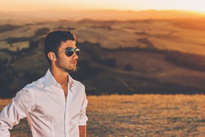 Portrait of man wearing sunglasses on field during sunset